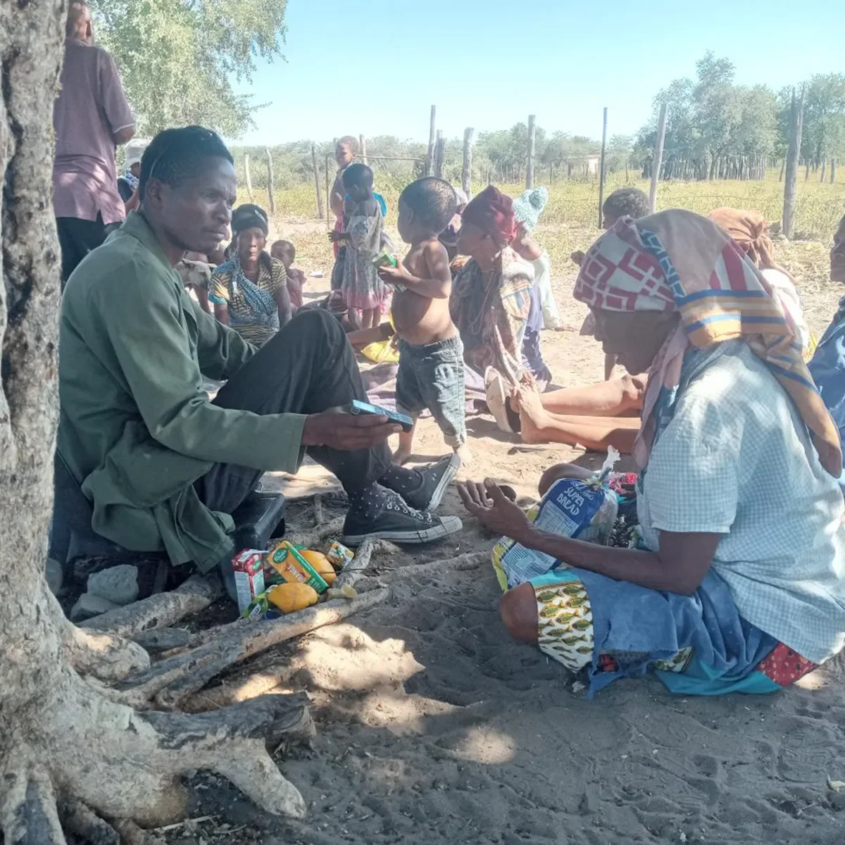 Community members gathered outdoors in conversation and shared activity in a rural setting.