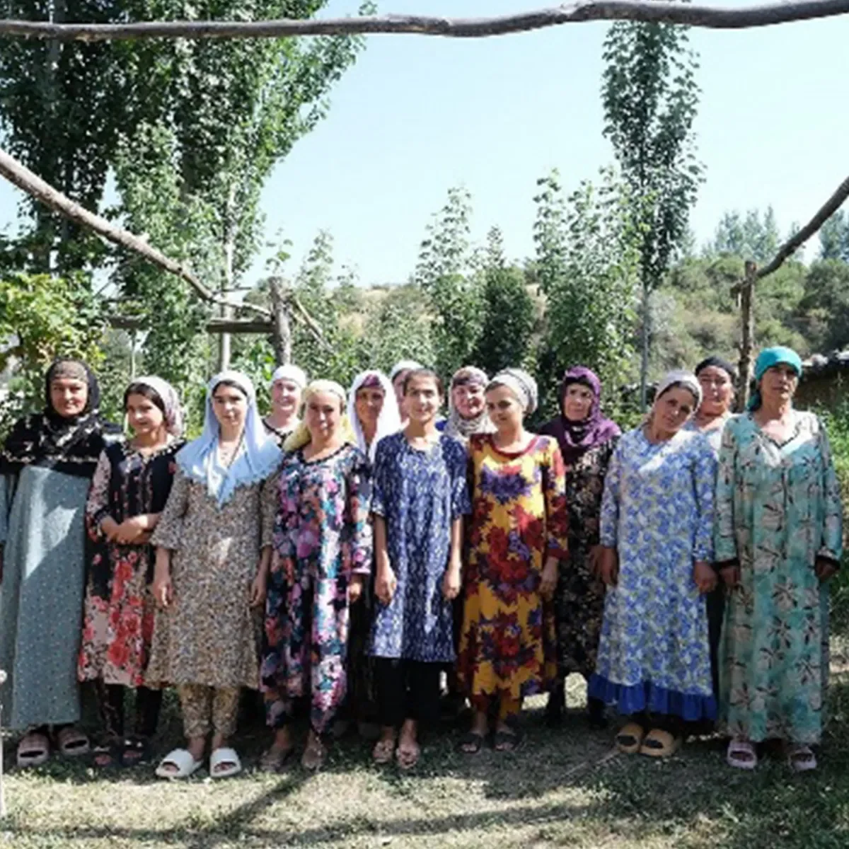 Large group of women standing together outdoors beneath trees during a community gathering or cultural exchange event.