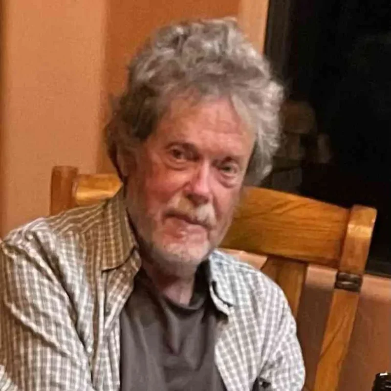 Portrait of an older man seated indoors during an interview or conversation.