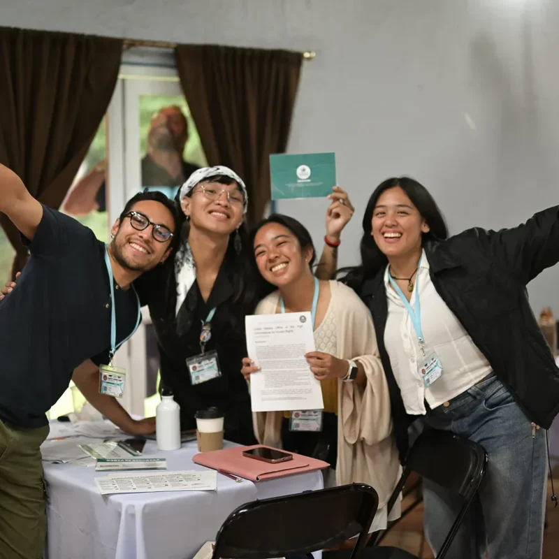 Group of smiling people taking a selfie indoors while holding certificates during a community or training event.
